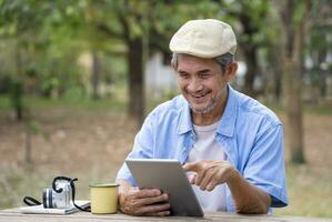 portrait happy senior man using online internet tablet searching direction for his journey while resting in the national park,concept of elderly people using technology for travel photo