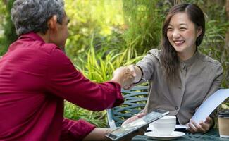 asian business woman handshaking to businessman at outdoors coffee shop while discuss work using a tablet,concept casual business,casual work,outdoors work,outdoor workspace photo