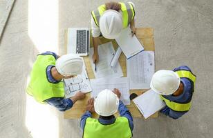 op view of engineers team meeting and discussing by using laptop,blueprint and documents on table in the building under construction,project manager consultation meeting with coworker photo