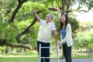 father and daughter enjoy walking in the park, senior man walking with walker, the father pointing index to something and laughing together. family relationship concept photo