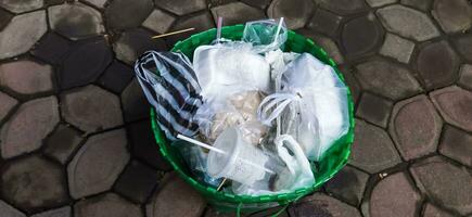 Waste basket full of rubbish, close-up. Disposable cups and other plastic waste in the trash can. photo