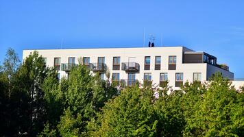 Modern apartment building and green trees. Ecological housing architecture. A modern residential building in the vicinity of trees. Ecology and green living in city, urban environment photo