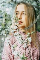 Blonde girl on a spring walk in the garden with cherry blossoms. Female portrait, close-up. A girl in a pink polka dot dress. photo