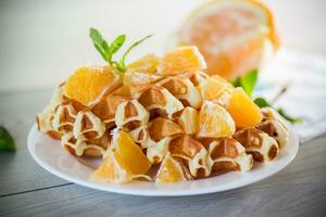 Cooked sweet Belgian waffles with oranges on the table. photo