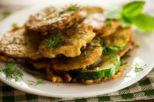 zucchini fried in circles in batter with herbs, in a plate . photo