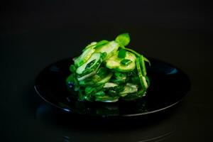 salad of fresh cucumbers with herbs and onions in a plate on a black background. photo