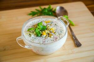 Cold soup with cucumbers, eggs, vegetables, yogurt and fresh herbs in a glass bowl . photo