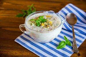 Cold soup with cucumbers, eggs, vegetables, yogurt and fresh herbs in a glass bowl . photo