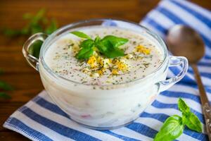 Cold soup with cucumbers, eggs, vegetables, yogurt and fresh herbs in a glass bowl . photo