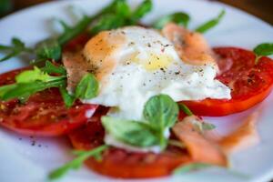 Cooked poached egg with herbs, lightly salted salmon and tomatoes with spices . photo