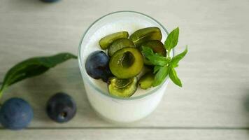 sweet homemade yogurt with fresh plum slices in a glass on a wooden table video