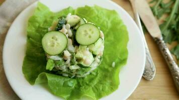 fresh summer salad with beans, rice, cucumbers and other vegetables in a plate on a wooden table. video