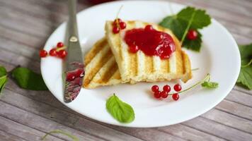 fried bread croutons for breakfast with redcurrant jam in a plate with berries on a wooden table. video