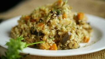 cooked bulgur with vegetables, carrots and dried mushrooms in a plate on a wooden table. video