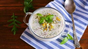 Cold soup with cucumbers, eggs, vegetables, yogurt and fresh herbs in a glass bowl on a wooden table. video