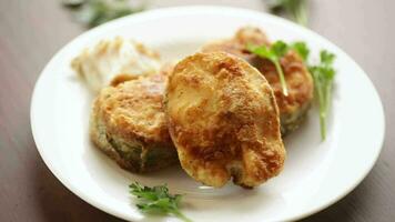 A piece of hake fish fried in a crispy crust, in a plate on a wooden table. video