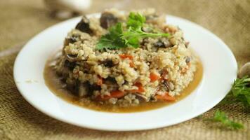 gekocht Bulgur mit Pilze, Möhren und Gemüse im ein Platte, auf ein hölzern Tisch. video