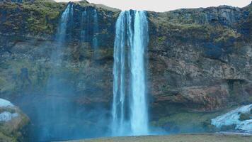 Beautiful seljalandsfoss waterfall in iceland circa March 2023, majestic river flowing down off of cliff. Icelandic cascade in nordic landscape with hills and mountains. Handheld shot. photo