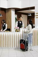 Tourist arrives at elegant resort and is preparing to do the check in at the reception. Female guest is welcomed by friendly and helpful staff at the front desk of cozy hotel. photo