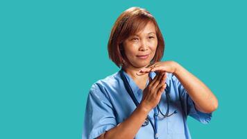 Close up shot of assertive asian nurse asking for timeout while at work. Clinic worker doing pause hand sign gesturing, wishing for break from job shift, isolated over studio background photo