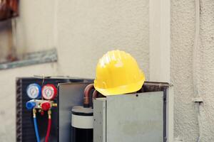 cerca arriba de amarillo proteccion casco en parte superior de fuera de Servicio externo aire acondicionador unidad en necesitar de reparar. al aire libre abrió hvac sistema con colector medidores y la seguridad engranaje foto