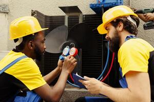 Meticulous wiremen expertly refilling freon in external air conditioner while using manifold measurement device to closely measure the pressure in HVAC system, ensuring perfect cooling performance photo