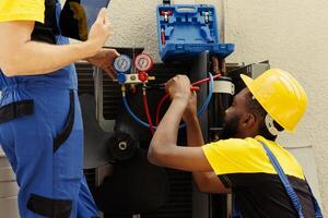 Technicians commissioned by home owner to do maintenance on air conditioner, fixing malfunctioning pressure measurement device. Engineers refilling refrigerant tank after servicing leak photo