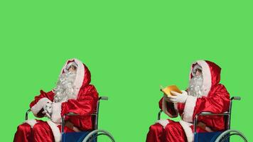 Santa claus in wheelchair reads book, portraying father christmas with physical disability. Adult in festive costume reading poetry or literature book, enjoying new hobby for culture and education. photo