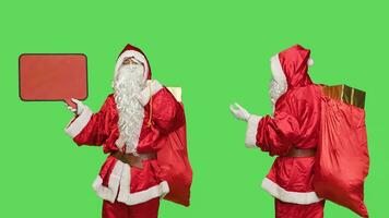 Santa character create advertisement using red speech bubble for marketing purposes, seasonal winter celebration. Father christmas showing empty billboard over greenscreen in studio. photo