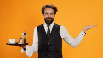 Confident waiter poses with tray in hand, standing against yellow background and working at restaurant. Catering industry worker with metal platter and towel providing outstanding luxury service. photo