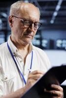 Old technician in cryptocurrency mining farm with specialized hardware using Blockchain technology. Fintech professional holding clipboard, inspecting asic rigs solving complex hashing operations photo