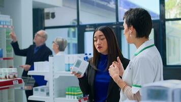 Shopper in modern chemist store asking helpful pharmacist for medical expertise. Licensed druggist helping customer trying to pick best pharmaceutical product to fight fever photo