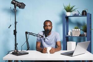 Blogger live streaming and broadcasting online for vlog video channel while looking at camera. African american man vlogger creating digital content and speaking on camera photo