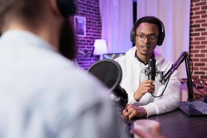 Podcast presenter having live discussion with man, streaming it online for audiences watching show. Influencer enjoying chat with guest, broadcasting in home studio living room with rgb lights photo