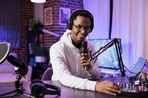 African american internet star recording show on camera, using sound equipment in studio. Portrait of smiling content creator talking to audience looking at camera and filming live broadcast photo