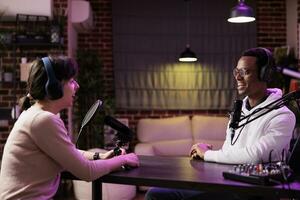 Man and woman broadcasting internet discussion on podcast episode, recording live for online spectators. Show host and guest talking in rgb lights ornate home studio livestream photo