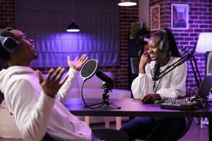 Online show host interviewing guest sharing funny stories about her life during live broadcast. Talking show interviewer using professional tools to record podcast, laughing together with woman photo