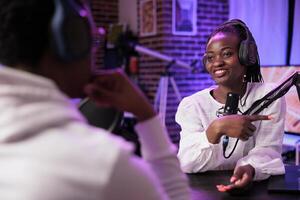 Online show host enjoying chat with african american woman sharing investment advice during business focused podcast. Talking show interviewer in home studio broadcasting interview live photo