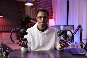 Portrait of technology vlogger comparing and reviewing over the ear headphones in living room studio. Knowledgeable content creator filming audiophiles channel vlog for streaming service photo