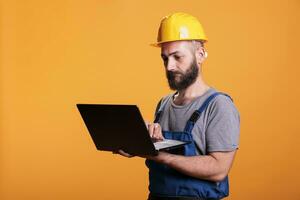 Handyman using laptop to browse internet website, looking for renovating inspiration. Construction site expert holding portable pc with wireless network, constructor at engineering job. photo