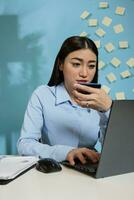 Corporate asian female employee using a laptop for Internet banking holding credit card. Businesswoman typing payment details sitting in the office, reviewing bank statement on secure website. photo