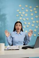 Woman showing a surprised expression, gesturing with hands in disbelief sitting at desk at workstation. Shocked female employee disconcerted by incident that happened at work. photo