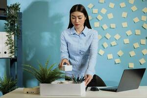 Angry fired employee putting her things in a box from office desk. Unemployed woman packing her things to take them home after a job inconvenience that caused contract termination. photo