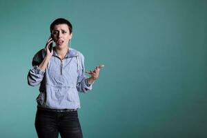 Brunette woman with short hair using smartphone to have remote conversation with friend standing over isolated background in studio. Cheerful woman smiling while having phone call discussion photo