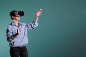Cheerful woman wearing virtual reality headset in 3d simulation using interactive equippment. Female adult with vr goggles having futuristic experience with videogame using modern digital technology. photo