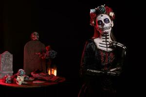 Young goddess of dead acting glamorous in studio, wearing traditional lady death skull make up and body art. Spooky female model with black la cavalera catrina halloween costume. photo