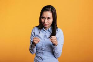 Defensive filipino fighter holding arms in self defense when encountering a life threat. Brave filipino woman clenching fists ready for boxing match, standing in studio over yellow background photo