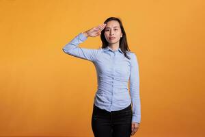 Filipino patriot woman doing military salute with hand over forehead, advertising honor and trustworthy respect in front of camera. Attractive young adult showing army soldier hello gesture in studio. photo