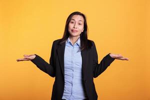 Doubtful filipino woman doing i dont know gesture, having problem understanding question. Confused model shrugging shoulders standing in studio over yellow background. Clueless expression photo