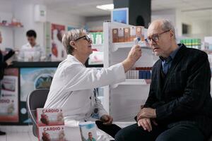 Apothecary worker holding infrared thermometer near elderly customer forehead, testing patient for fever. Old customer measuring body temperature in drugstore, getting common cold diagnosis photo